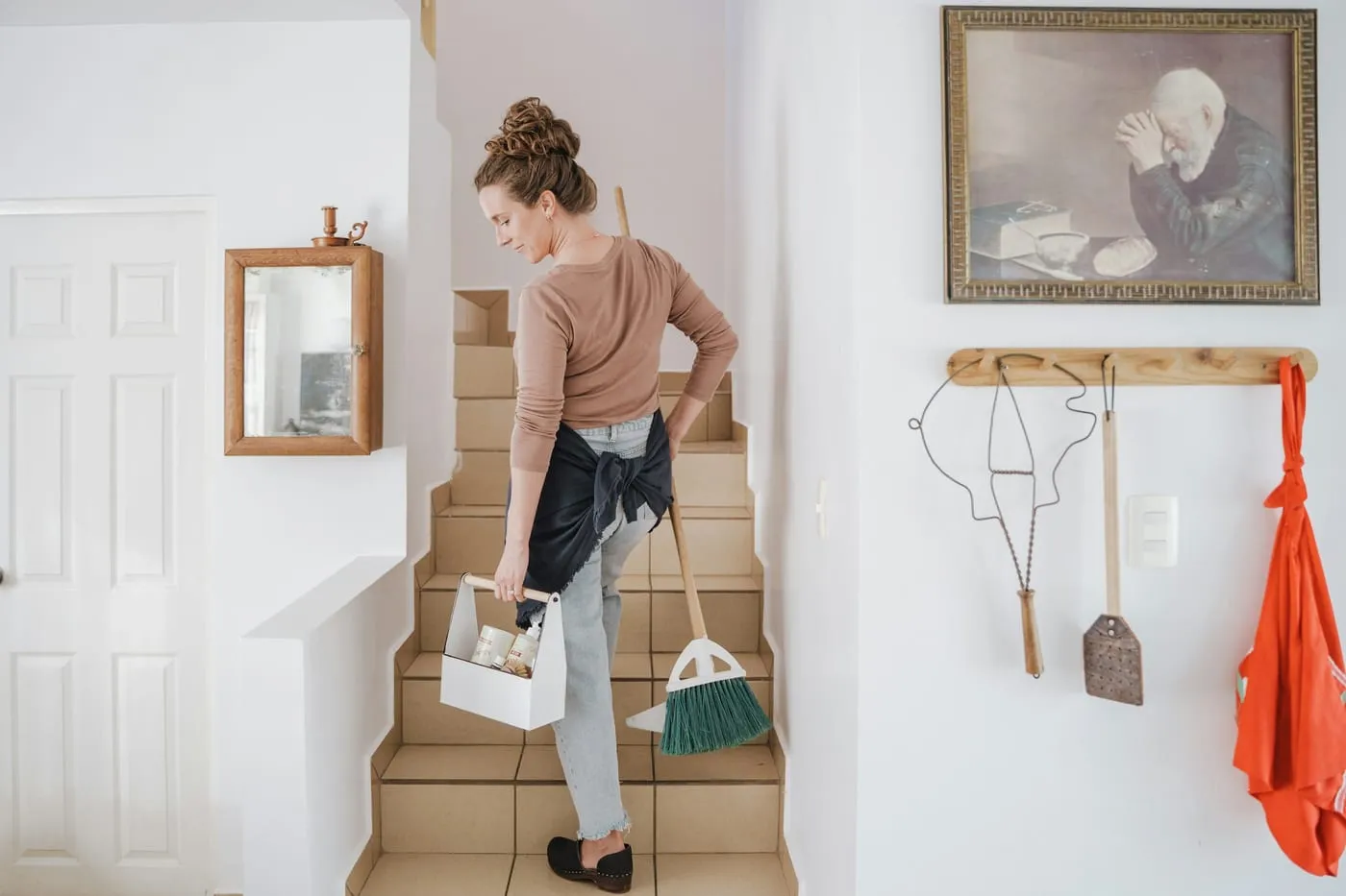 Préposée à l’entretien transportant son panier de produits et son balai dans une maison.